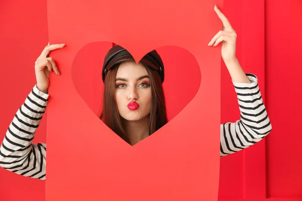 Hermosa mujer joven sosteniendo papel con el corazón cortado en el fondo de color. Celebración de San Valentín —  Fotos de Stock