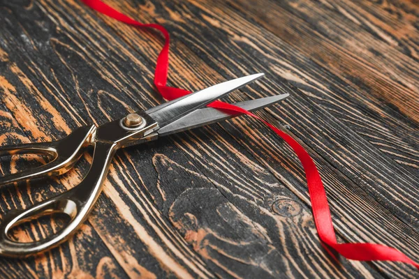 Scissors and red ribbon on wooden background