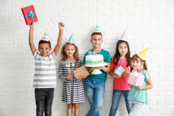 Little children with Birthday cake and gifts on white brick background — Stock Photo, Image