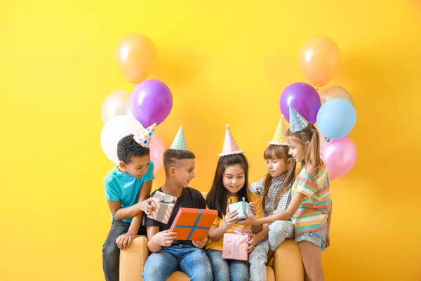 Маленькі діти вітають дівчину з подарунками на день народження на кольоровому фоні — стокове фото