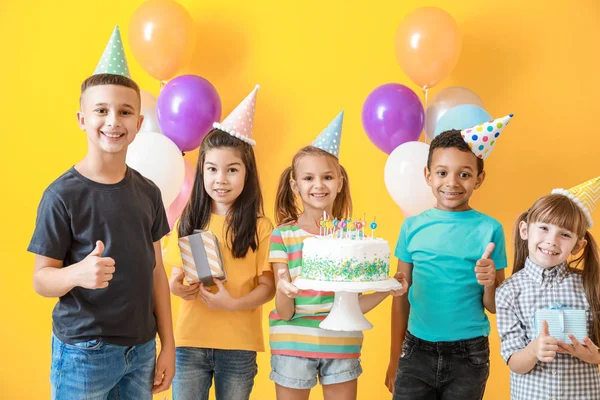 Niños pequeños con pastel de cumpleaños mostrando gesto de pulgar hacia arriba en el fondo de color —  Fotos de Stock