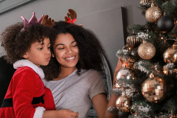 Glückliche afrikanisch-amerikanische Frau und ihre kleine Tochter in der Nähe des schönen Weihnachtsbaums zu Hause — Stockfoto