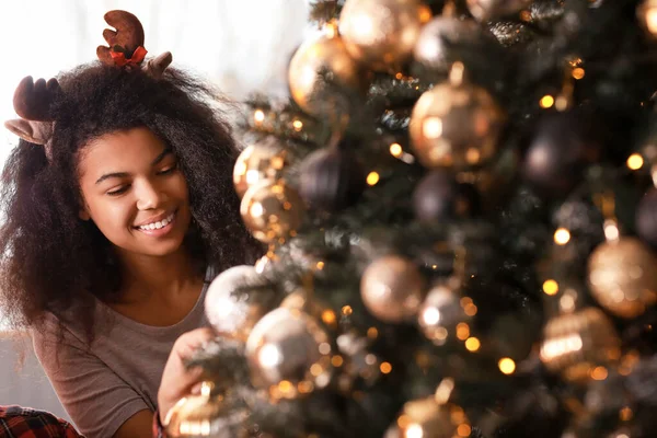 Happy African-American woman decorating Christmas tree at home — Stock Photo, Image