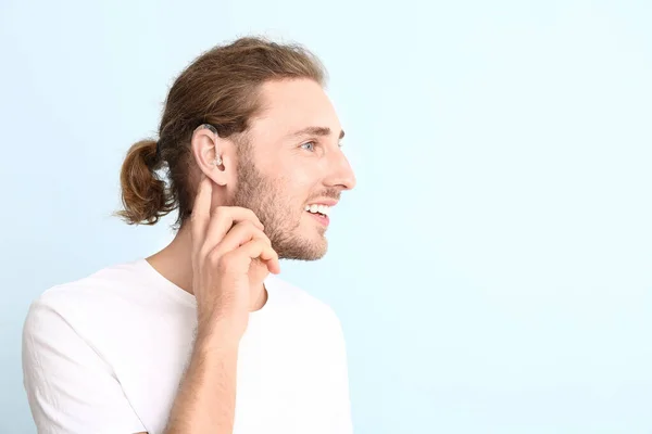 Hombre joven con audífono sobre fondo de color — Foto de Stock