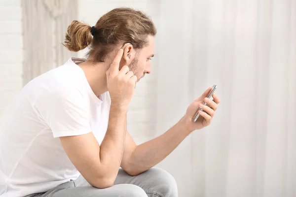 Mladý muž s naslouchátkem pomocí mobilního telefonu doma — Stock fotografie