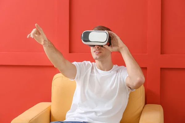 Junger Mann mit Virtual-Reality-Brille sitzt im Sessel auf farbigem Hintergrund — Stockfoto