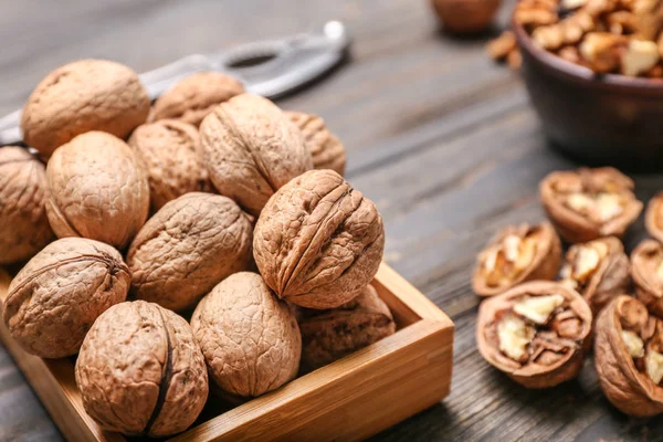 Box with tasty walnuts on wooden background