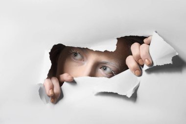 Yaratıcı makyajlı güzel bir kadın kağıttaki delikten bakıyor.