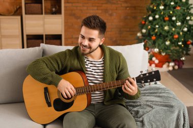 Noel arifesinde evde gitar çalan yakışıklı genç adam.