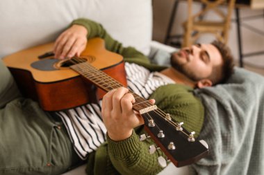 yakışıklı genç adam evde gitar çalıyor.