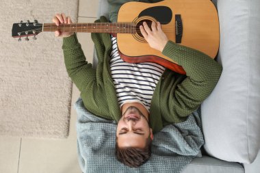 yakışıklı genç adam evde gitar çalıyor.