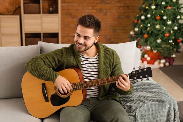 Bonito jovem tocando guitarra em casa na véspera de Natal — Fotografia de Stock