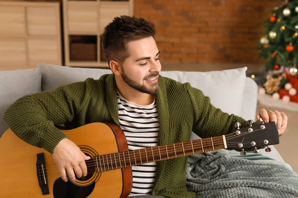 Noel arifesinde evde gitar çalan yakışıklı genç adam.