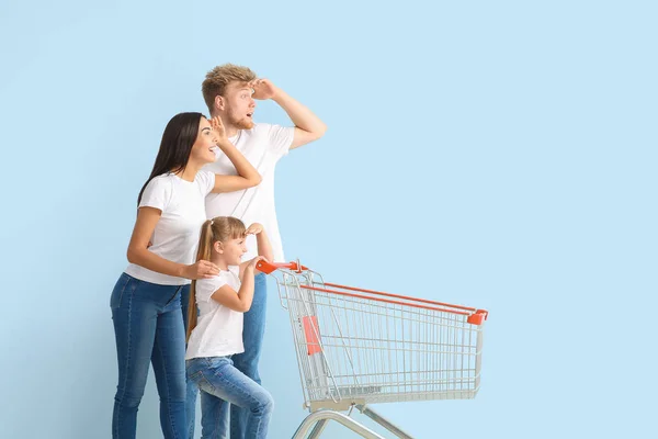 Family with empty shopping cart on color background — Stock Photo, Image