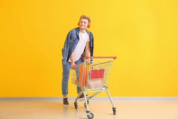 Jongeman met winkelwagen in de buurt van kleur muur — Stockfoto