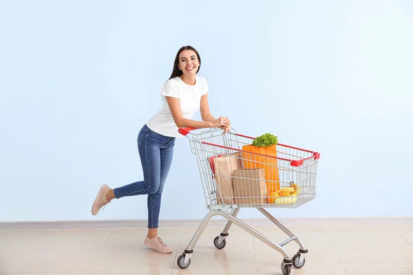 Mladá žena s nákupním vozíkem u barevné stěny — Stock fotografie