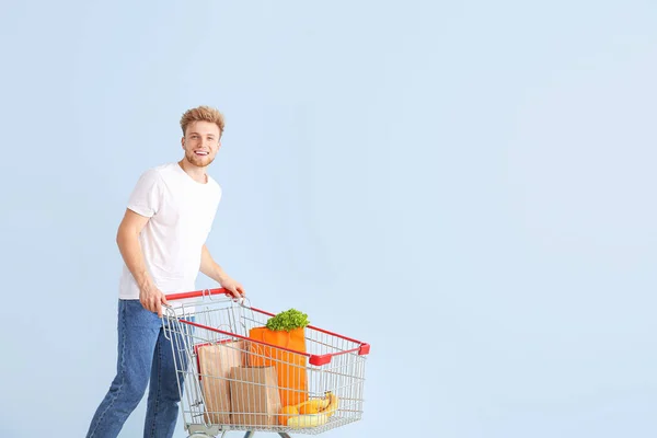 Fiatal férfi bevásárlókosár színes háttér — Stock Fotó
