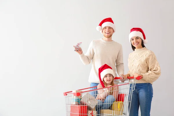 Família com carrinho de compras cheio de presentes de Natal no fundo claro — Fotografia de Stock