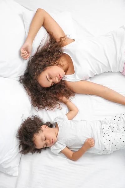 Liten afro-amerikansk flicka med mamma sover i sängen — Stockfoto