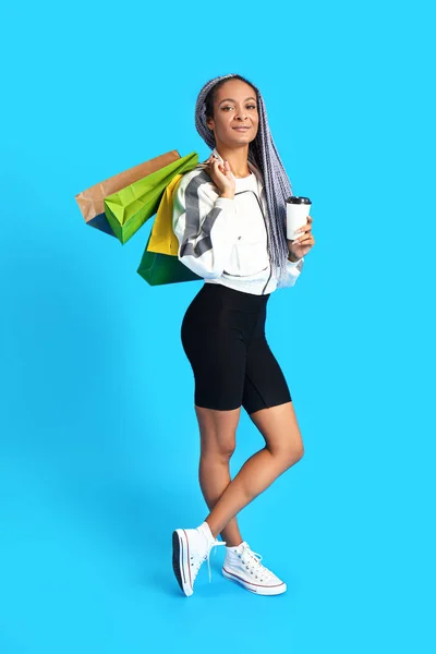 Afrikai-amerikai nő bevásárló táskák és kávé színes háttér — Stock Fotó