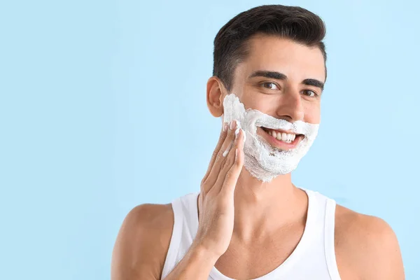 Hezký mladý muž použití pěny na holení na barevném pozadí — Stock fotografie
