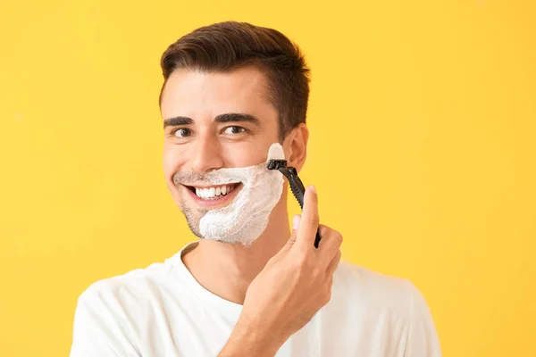 Handsome young man shaving against on color background — Stock Photo, Image