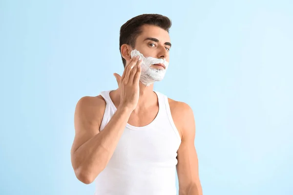 Hombre joven guapo aplicando espuma de afeitar contra el fondo de color — Foto de Stock