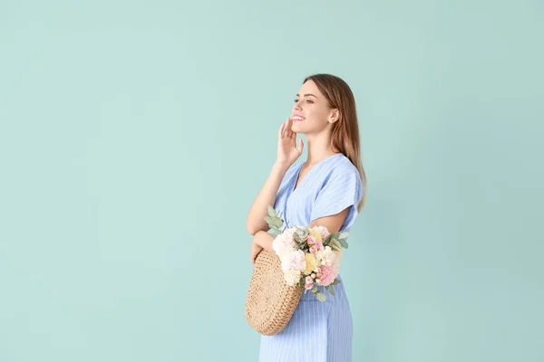Beautiful young woman with bag and bouquet of carnation flowers on color background — Stock Photo, Image