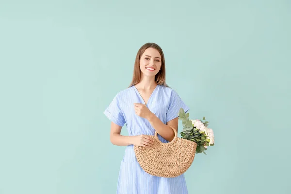 Beautiful young woman with bag and bouquet of carnation flowers on color background — Stock Photo, Image