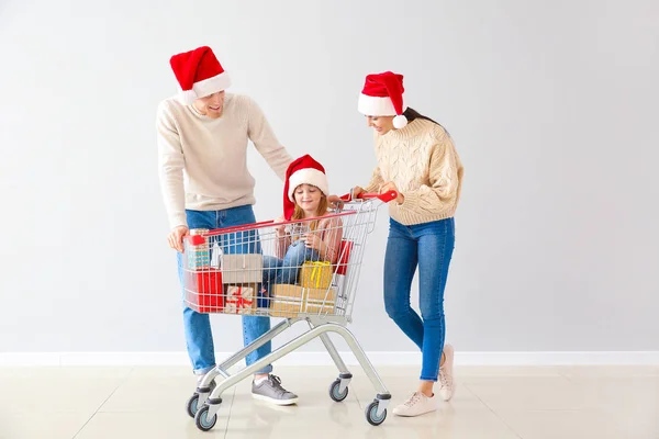 Family with shopping cart full of Christmas gifts near light wall — Stock Photo, Image