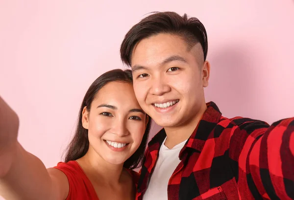Portrait of happy young Asian couple taking selfie on color background — Stock Photo, Image