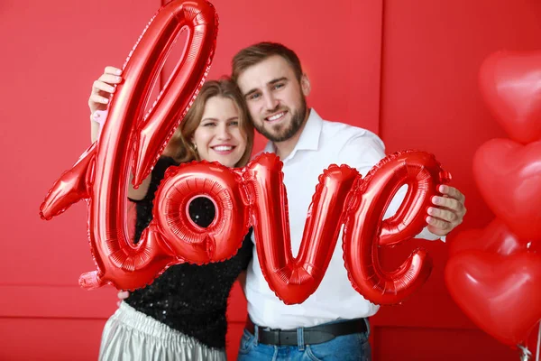 Glückliches junges Paar mit Luftballon in Form von Wortliebe auf farbigem Hintergrund. Valentinstag-Feier — Stockfoto