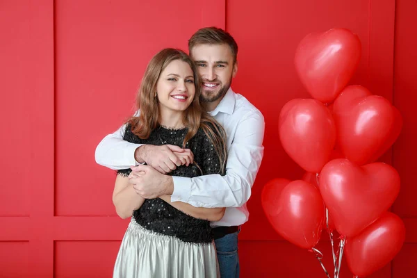 Pasangan muda bahagia dengan balon berbentuk hati di latar belakang warna. Hari Valentine perayaan — Stok Foto
