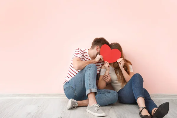 Happy young couple with red heart sitting near color wall. Valentine's Day celebration — Stock Photo, Image