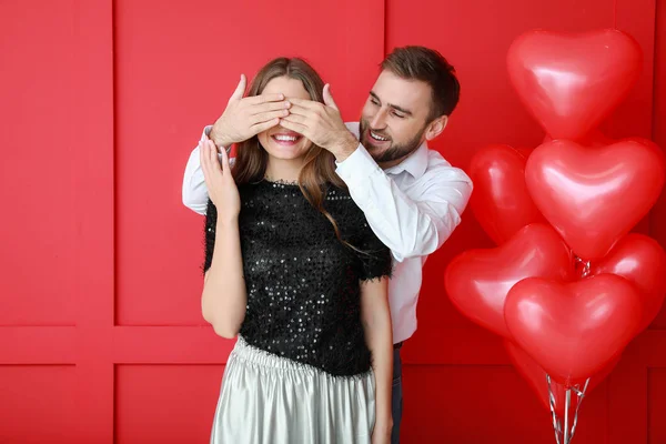 Šťastný mladý pár s balónky ve tvaru srdce na barevném pozadí. Valentýnská oslava — Stock fotografie