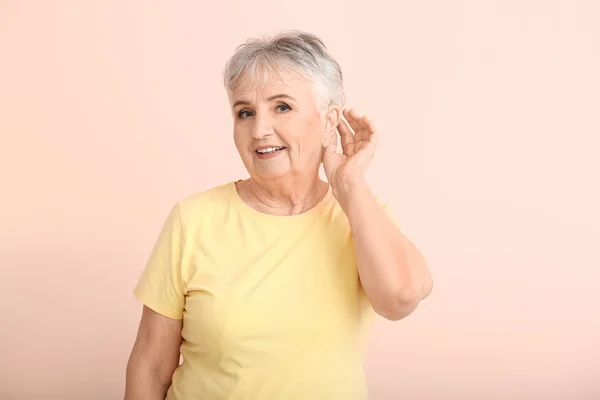 Senior woman with hearing aid on color background — Stock Photo, Image