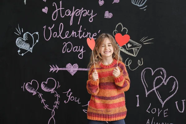Niedliches kleines Mädchen mit Papierherzen in der Nähe dunkler Wände. Valentinstag-Feier — Stockfoto