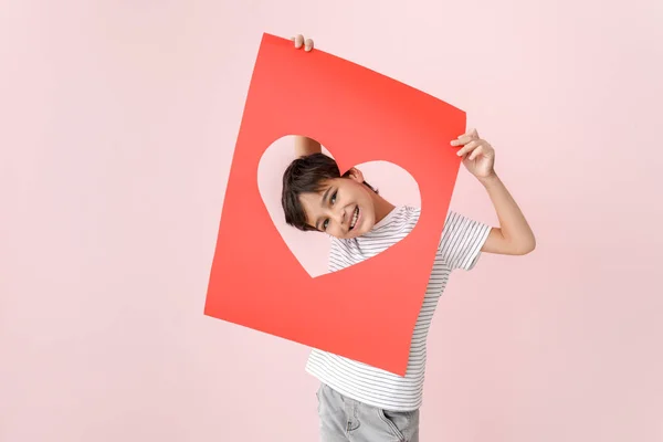 Ragazzino carino che tiene il foglio di carta con foro a forma di cuore sullo sfondo a colori. Festa di San Valentino — Foto Stock