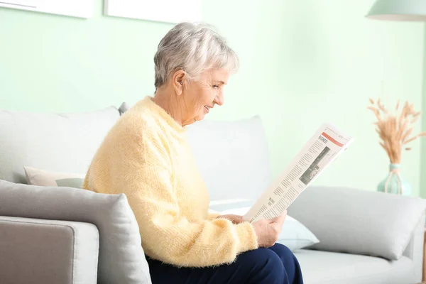 Senior woman with hearing aid reading newspaper at home — Stock Photo, Image