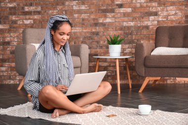 Evde online alışveriş için dizüstü bilgisayar kullanan Afro-Amerikalı bir kadın.