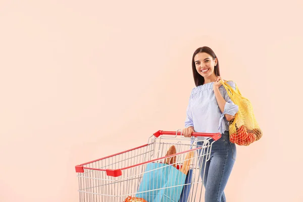 Jovem com carrinho de compras em fundo de cor — Fotografia de Stock