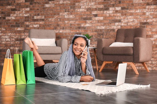 Afroameričanka mluvící telefonicky při použití přenosného počítače pro online nakupování doma — Stock fotografie