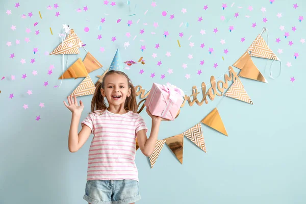 Glückliches kleines Mädchen mit Geburtstagsgeschenk auf farbigem Hintergrund — Stockfoto