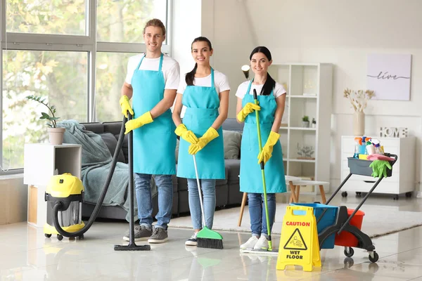 Team van conciërges met schoonmaakmiddelen in de kamer — Stockfoto