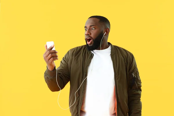 Emotional African-American man listening to music on color background — Stock Photo, Image