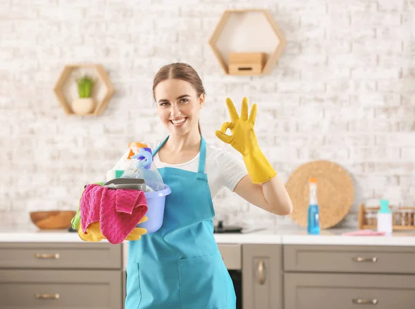 Vrouwelijke conciërge met schoonmaakspullen met OK gebaar in de keuken — Stockfoto