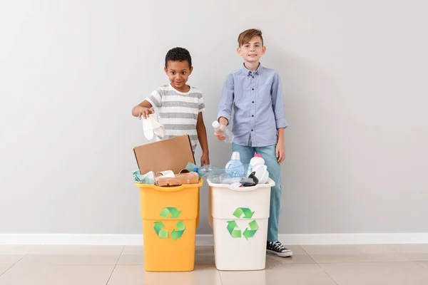 Niños pequeños y contenedores con basura cerca de la pared de luz. Concepto de reciclaje — Foto de Stock