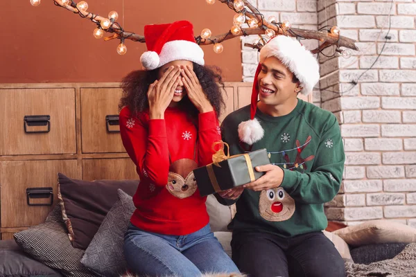 Happy African-American man giving Christmas present to his wife at home — Stock Photo, Image