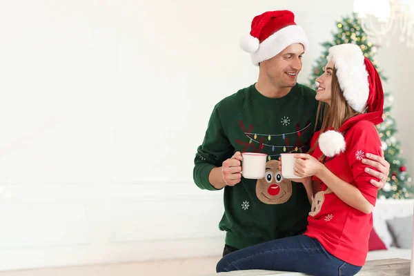 Jovem casal feliz com xícaras de chocolate quente na véspera de Natal em casa — Fotografia de Stock