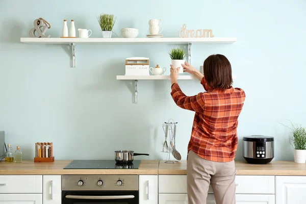 Mujer poniendo planta de interior en estante de la cocina —  Fotos de Stock